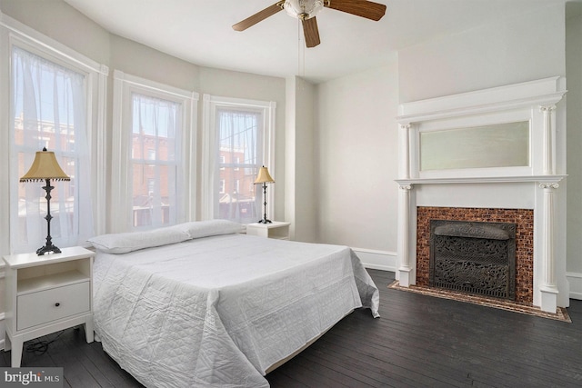 bedroom with a tile fireplace, dark wood-type flooring, and ceiling fan