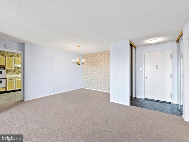 spare room with an inviting chandelier, dark carpet, and a textured ceiling