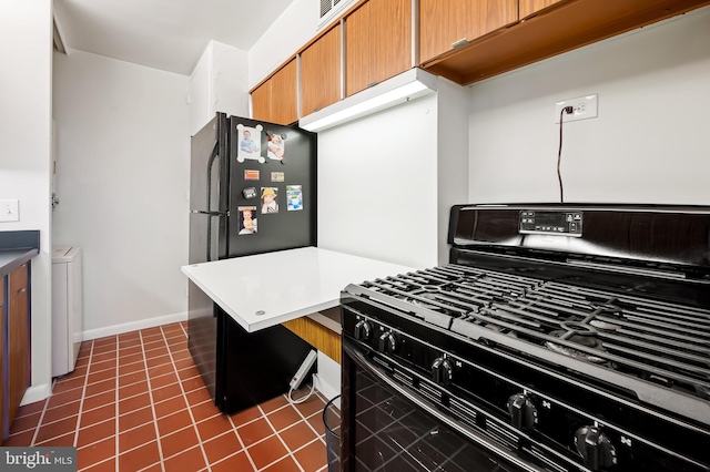 kitchen with dark tile patterned floors, gas stove, and stainless steel refrigerator