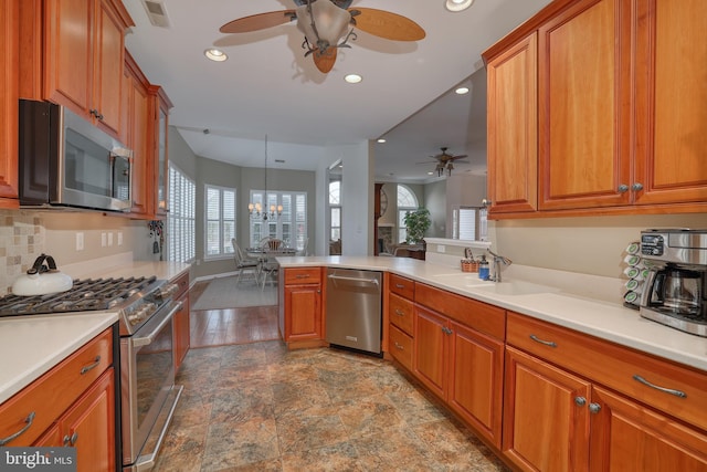 kitchen with sink, hanging light fixtures, stainless steel appliances, ceiling fan with notable chandelier, and kitchen peninsula