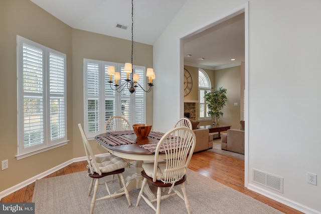 dining room with an inviting chandelier, lofted ceiling, a fireplace, and light wood-type flooring