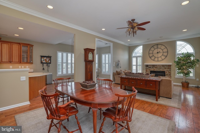 dining area featuring crown molding, a fireplace, light hardwood / wood-style floors, and a healthy amount of sunlight