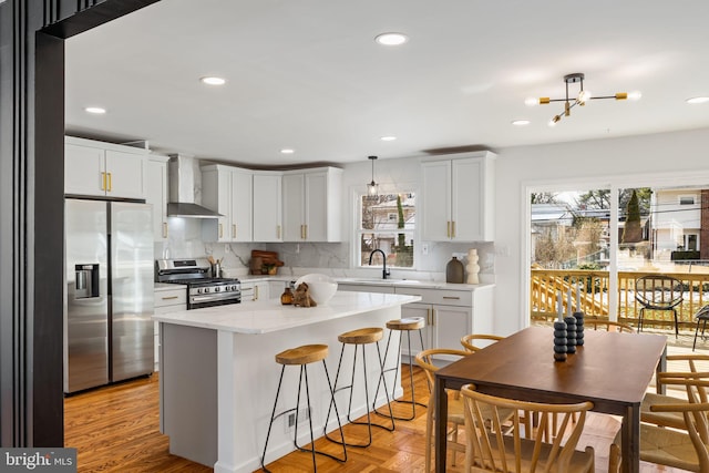 kitchen with sink, white cabinetry, decorative light fixtures, stainless steel appliances, and wall chimney range hood