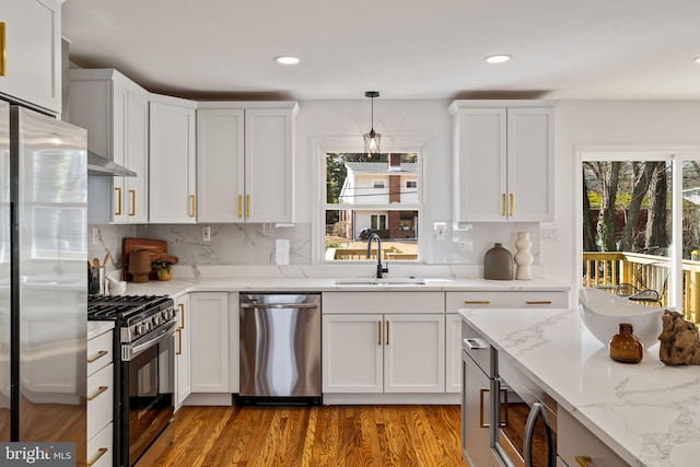 kitchen with appliances with stainless steel finishes, pendant lighting, sink, white cabinets, and light stone countertops