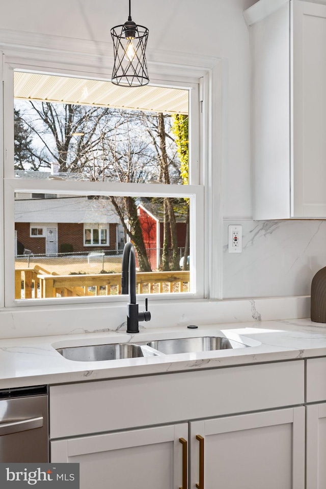 interior details featuring light stone counters, sink, decorative light fixtures, and white cabinetry