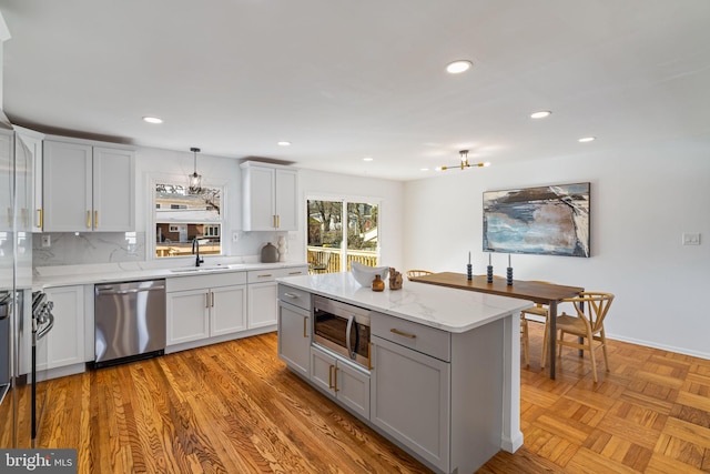 kitchen featuring sink, hanging light fixtures, stainless steel appliances, light stone counters, and tasteful backsplash