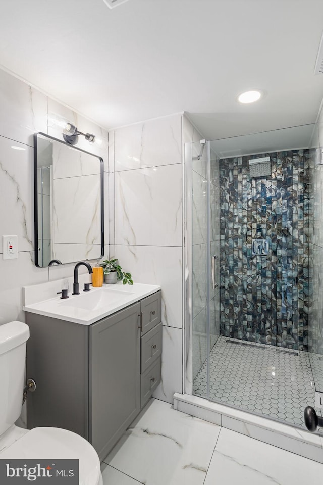 bathroom with a shower with door, vanity, tile walls, and toilet