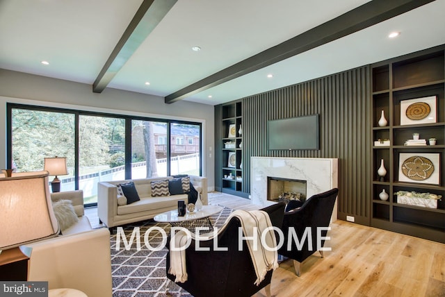 living room with a premium fireplace, beam ceiling, built in features, and light hardwood / wood-style flooring