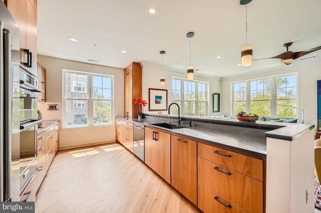 kitchen with a sink, stainless steel appliances, decorative light fixtures, light wood-style flooring, and a peninsula