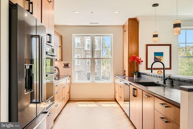 kitchen featuring stainless steel appliances, dark countertops, a sink, light wood-type flooring, and pendant lighting
