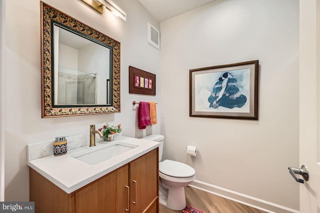 bathroom with wood finished floors, toilet, vanity, baseboards, and visible vents