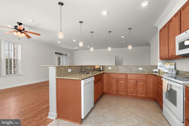 kitchen with brown cabinets, decorative light fixtures, a peninsula, white appliances, and ornamental molding