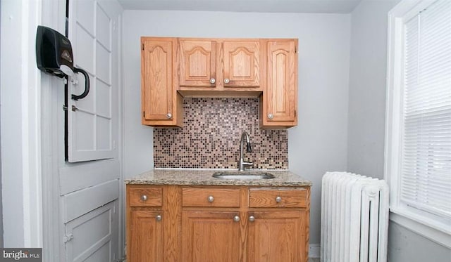 kitchen featuring tasteful backsplash, radiator, sink, and light stone counters