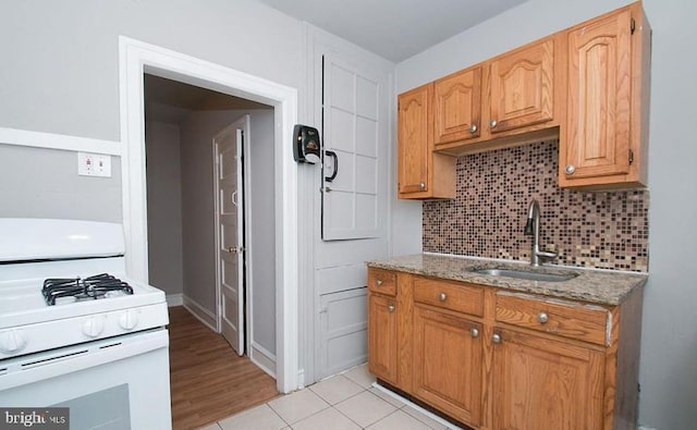 kitchen with sink, decorative backsplash, white range with gas cooktop, light tile patterned floors, and light stone countertops