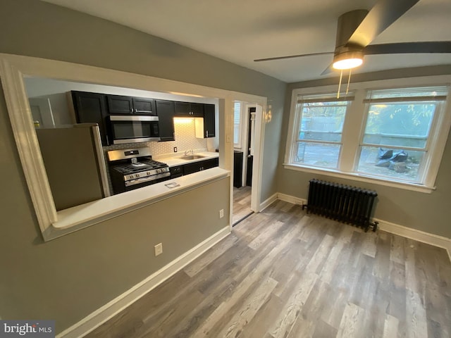 kitchen featuring sink, radiator heating unit, stainless steel appliances, tasteful backsplash, and light hardwood / wood-style floors