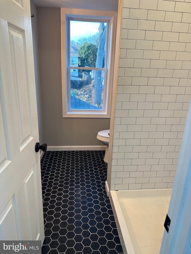 full bathroom with a stall shower, tile patterned floors, toilet, and baseboards