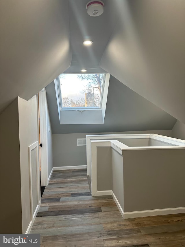 additional living space with baseboards, visible vents, vaulted ceiling, and wood finished floors