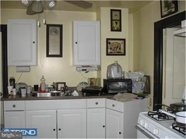 kitchen featuring a ceiling fan, white gas range oven, white cabinetry, and a sink