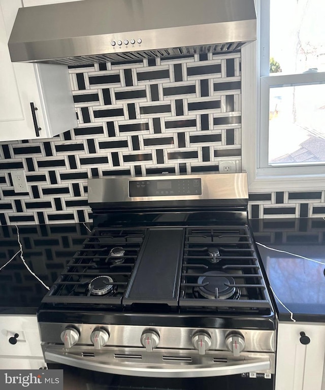 room details featuring white cabinetry, ventilation hood, decorative backsplash, stainless steel gas stove, and dark countertops