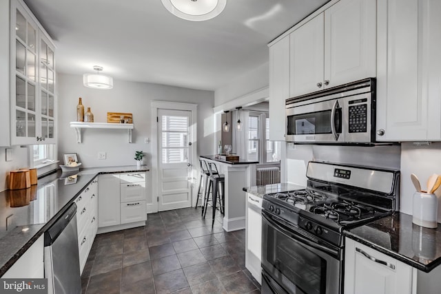 kitchen with white cabinetry, dark tile patterned flooring, stainless steel appliances, and dark stone counters