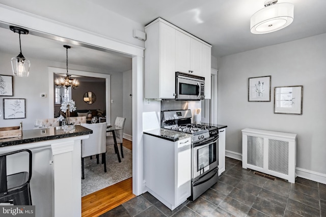 kitchen featuring dark stone countertops, hanging light fixtures, radiator heating unit, stainless steel appliances, and white cabinets