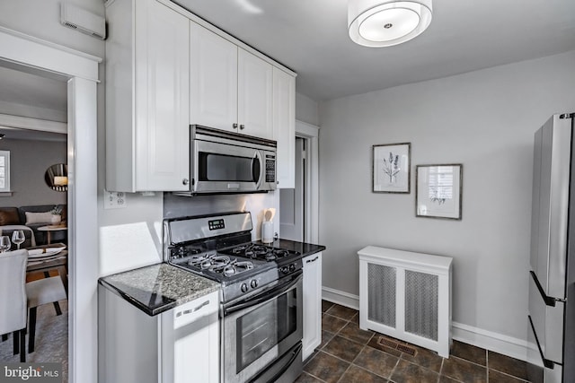 kitchen with appliances with stainless steel finishes, radiator, a wall unit AC, dark stone counters, and white cabinets