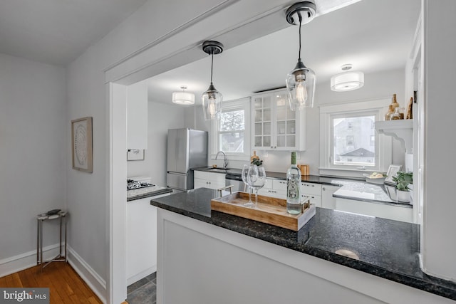 kitchen featuring hanging light fixtures, appliances with stainless steel finishes, kitchen peninsula, dark stone counters, and white cabinets