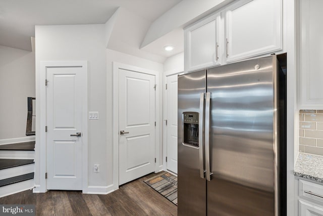 kitchen with light stone counters, dark hardwood / wood-style floors, stainless steel fridge, white cabinets, and backsplash