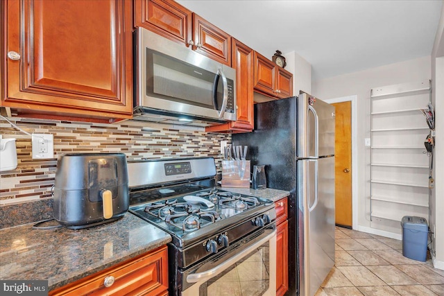 kitchen featuring light tile patterned flooring, appliances with stainless steel finishes, decorative backsplash, and dark stone counters