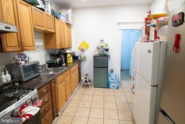 kitchen featuring sink, light tile patterned floors, stainless steel gas stove, fridge, and white refrigerator