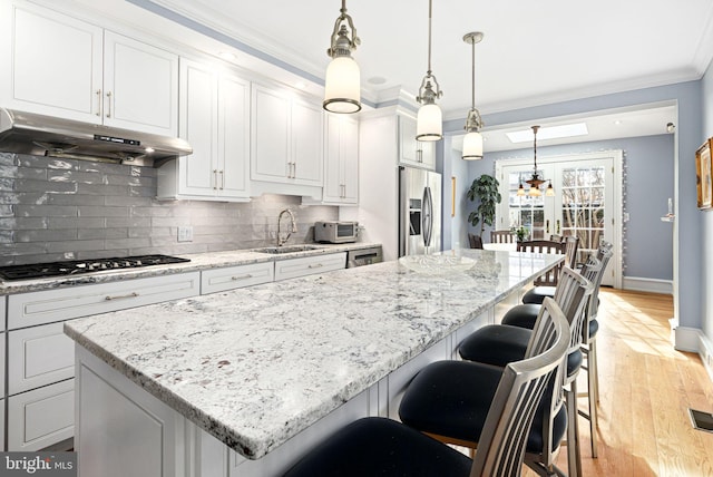 kitchen with pendant lighting, sink, white cabinetry, stainless steel appliances, and a center island