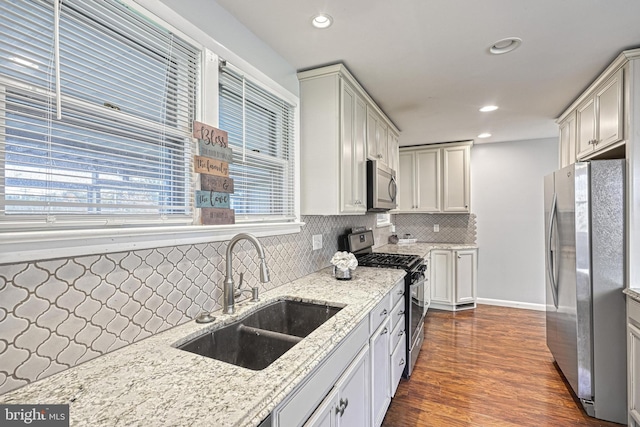 kitchen featuring appliances with stainless steel finishes, sink, decorative backsplash, light stone countertops, and dark wood-type flooring