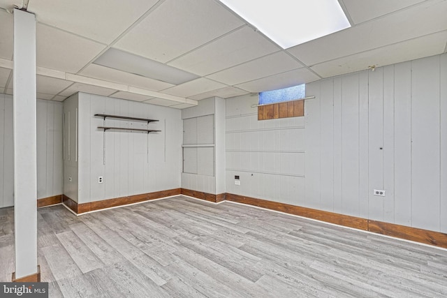 basement with a paneled ceiling, wooden walls, and light wood-type flooring