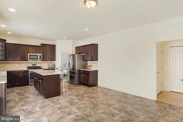 kitchen featuring dark brown cabinetry, appliances with stainless steel finishes, a kitchen breakfast bar, a kitchen island, and decorative backsplash