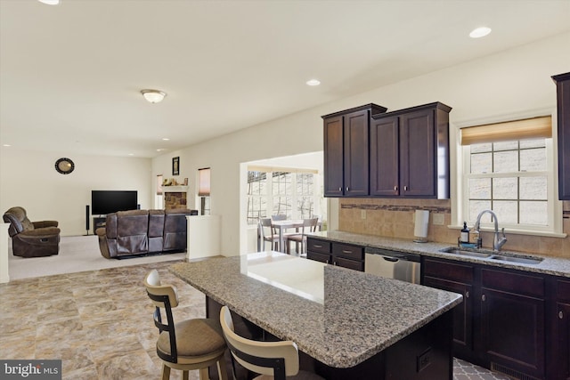 kitchen featuring sink, a breakfast bar, dishwasher, light stone countertops, and a kitchen island