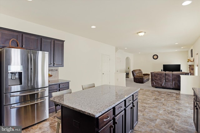 kitchen with a kitchen island, dark brown cabinets, a breakfast bar area, and stainless steel fridge