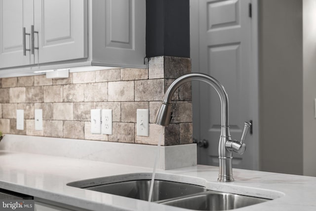 details featuring white cabinetry, sink, dishwashing machine, decorative backsplash, and light stone countertops