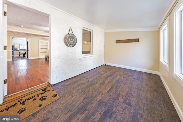 spare room with ornamental molding, brick wall, baseboards, and wood finished floors