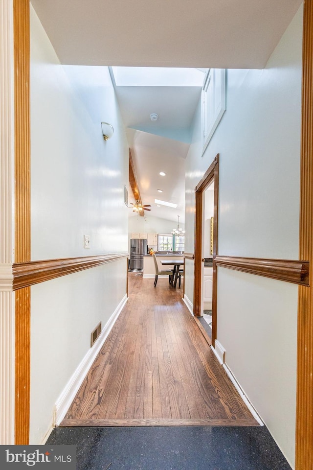 hallway with wood finished floors, baseboards, and visible vents