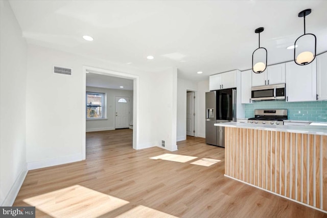 kitchen with white cabinetry, appliances with stainless steel finishes, pendant lighting, light hardwood / wood-style floors, and backsplash