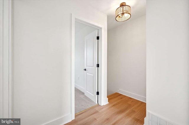 corridor with an inviting chandelier and light hardwood / wood-style flooring