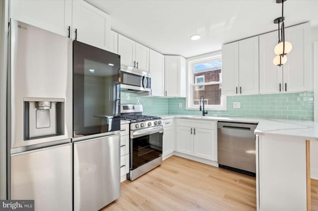 kitchen with tasteful backsplash, white cabinets, hanging light fixtures, light stone counters, and stainless steel appliances