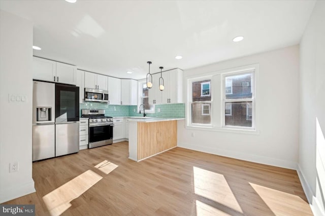 kitchen with sink, appliances with stainless steel finishes, white cabinetry, decorative light fixtures, and kitchen peninsula