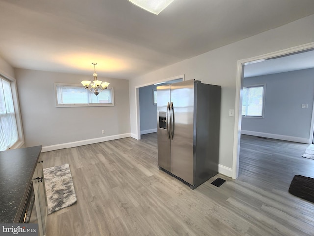 kitchen featuring light wood-style flooring, dark countertops, hanging light fixtures, and stainless steel refrigerator with ice dispenser