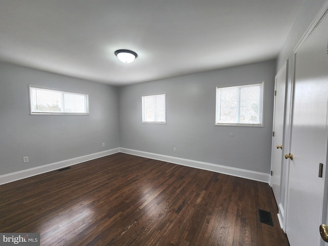 empty room featuring dark wood-style floors, baseboards, and visible vents