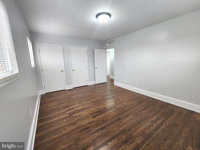 unfurnished bedroom featuring baseboards, visible vents, dark wood finished floors, and multiple closets