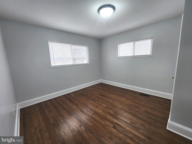 empty room featuring plenty of natural light, visible vents, baseboards, and dark wood finished floors