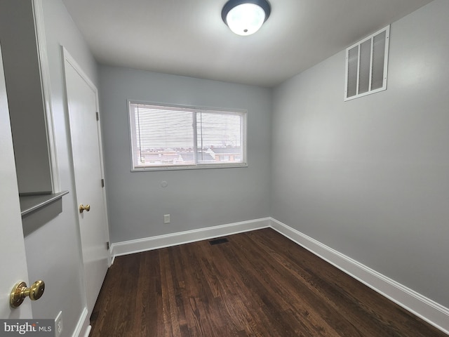 empty room with dark wood-style flooring, visible vents, and baseboards