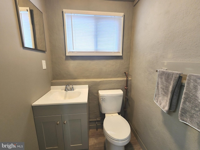 half bath featuring toilet, a textured wall, and vanity