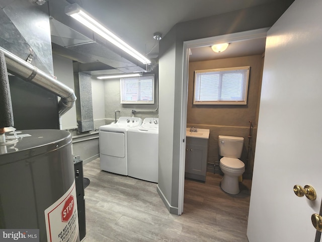 clothes washing area with gas water heater, laundry area, a sink, wood finished floors, and washer and clothes dryer